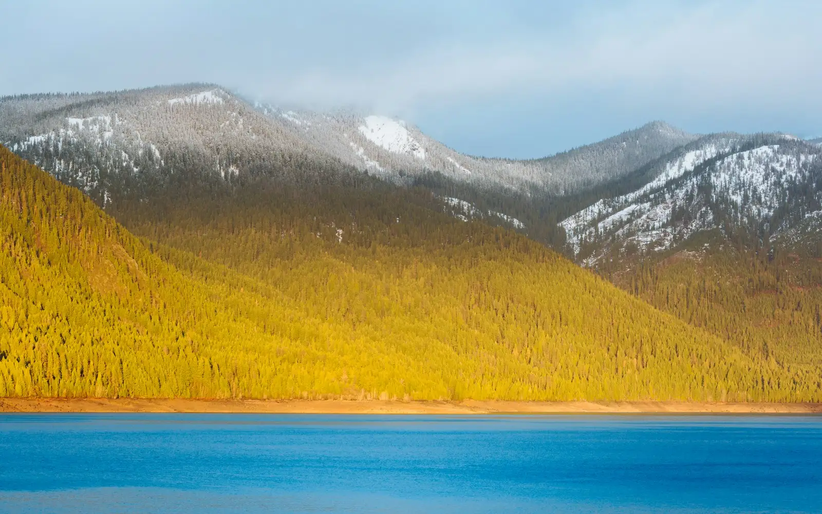 A calm alpine lake reflecting snow-capped mountains at sunrise near Cle Elum, Washington.