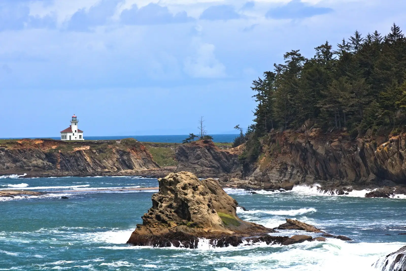 Cape Arago Lighthouse on a headland above a sea stack and surf near Coos Bay, Oregon.