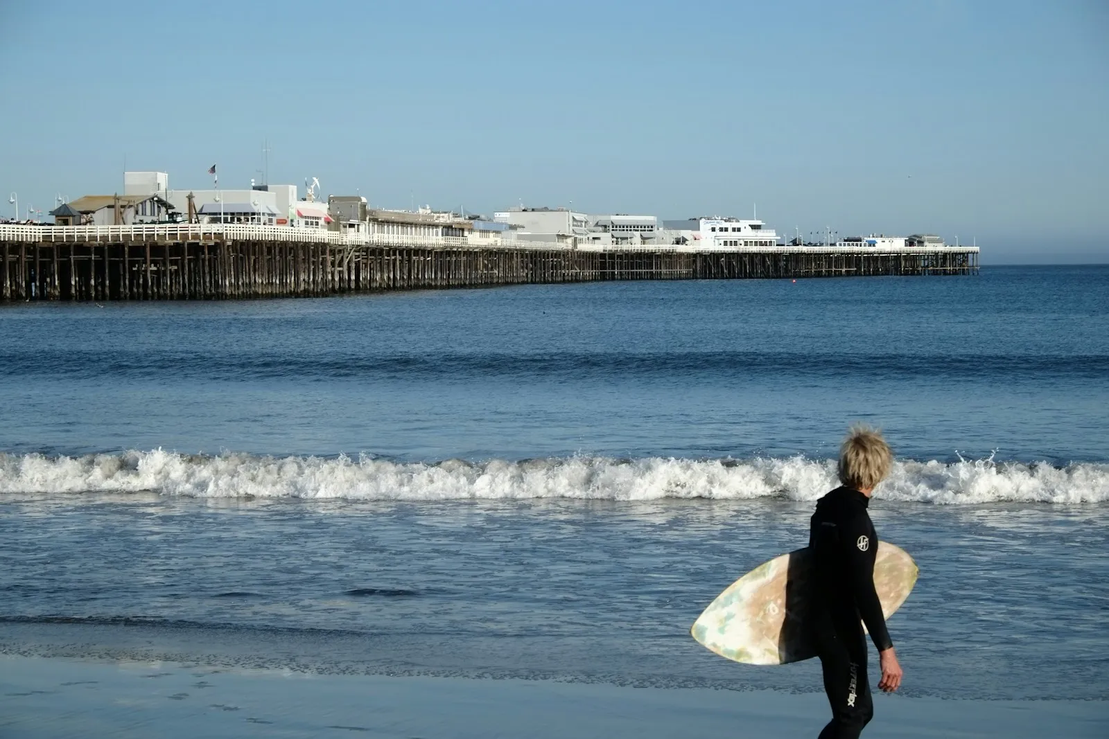 A person carrying a surfboard on the beach at Santa Cruz, California.